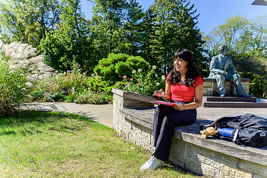 A female student doing homework by the outdoor Lincoln Plaza Statue.
