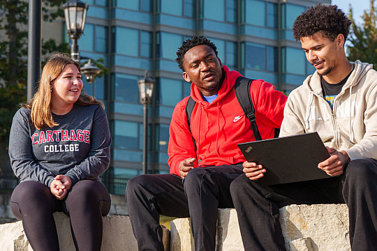 Three students sitting on rocks outside.