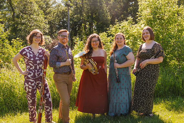 A group of musicians holding their instruments in a wooded outdoors area.