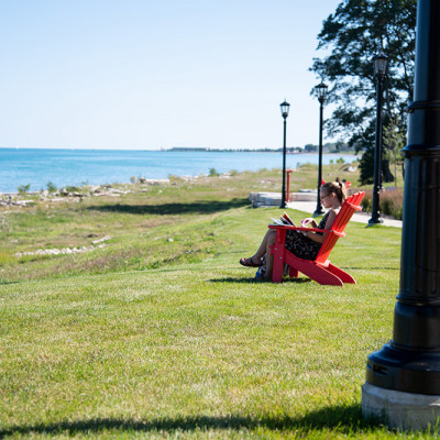 A student studies in a red Adirondack chair with a lake view.