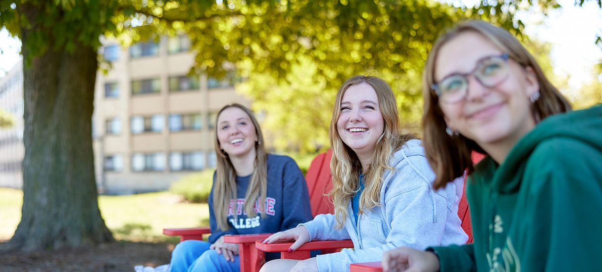 Two students unwind lakeside in Carthage's famous red adirondack chairs.