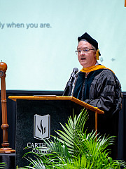 A robed professor speaks in front of a screen displaying the text Ready when you are.